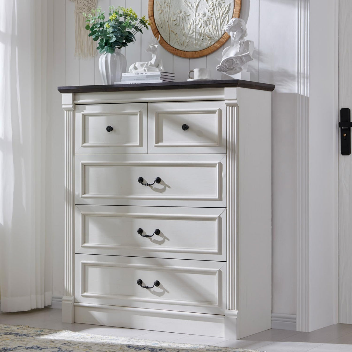 Three-quarter view of a tall antique white chest of drawers with dark top and decorative hardware.