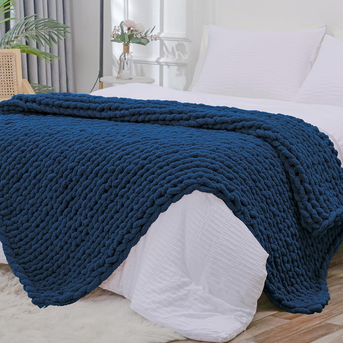 Deep navy chunky knit throw folded over the foot of a white bed, showing textured knit pattern.