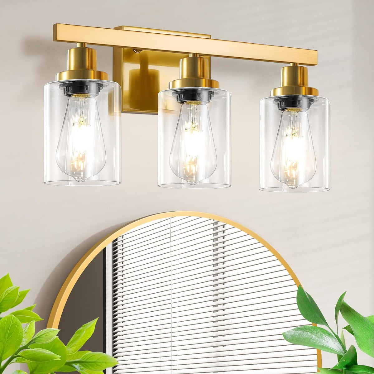 Three-light gold vanity fixture with clear cylindrical shades above a round mirror.
