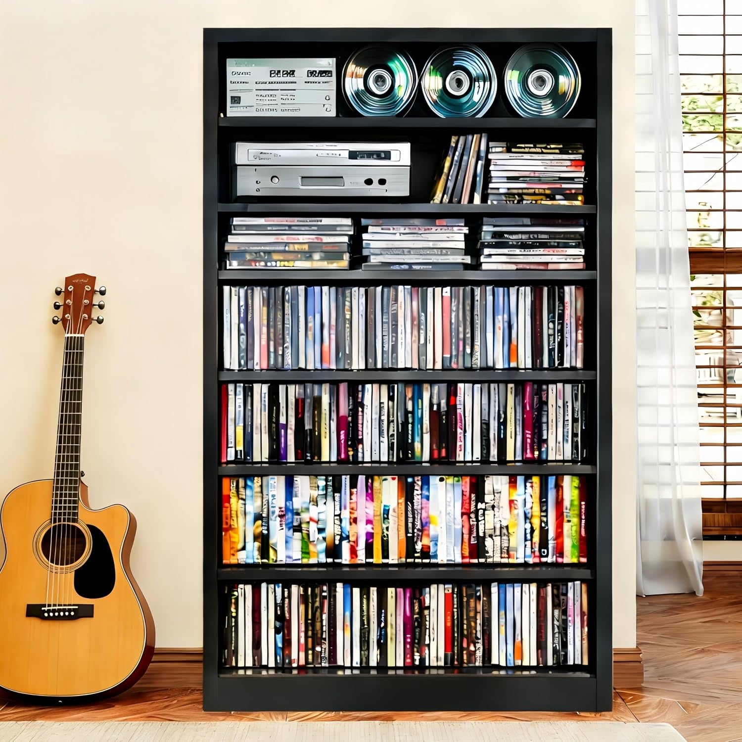 Black 7-tier metal media cabinet filled with CDs and DVDs, front view in a living room setting with a guitar.