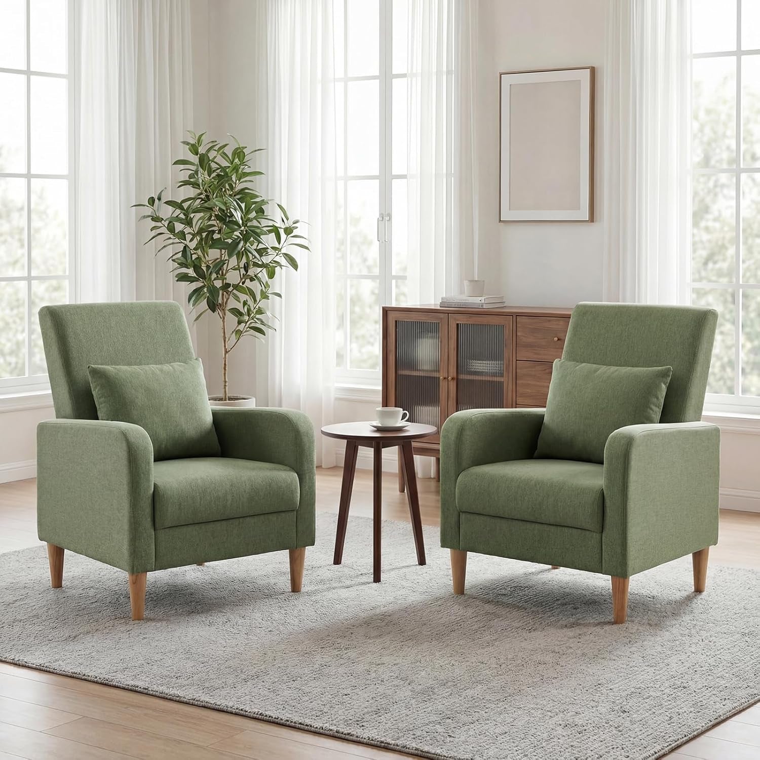 Two mid-century upholstered accent chairs in muted green flanking a small round wooden table in a sunlit room