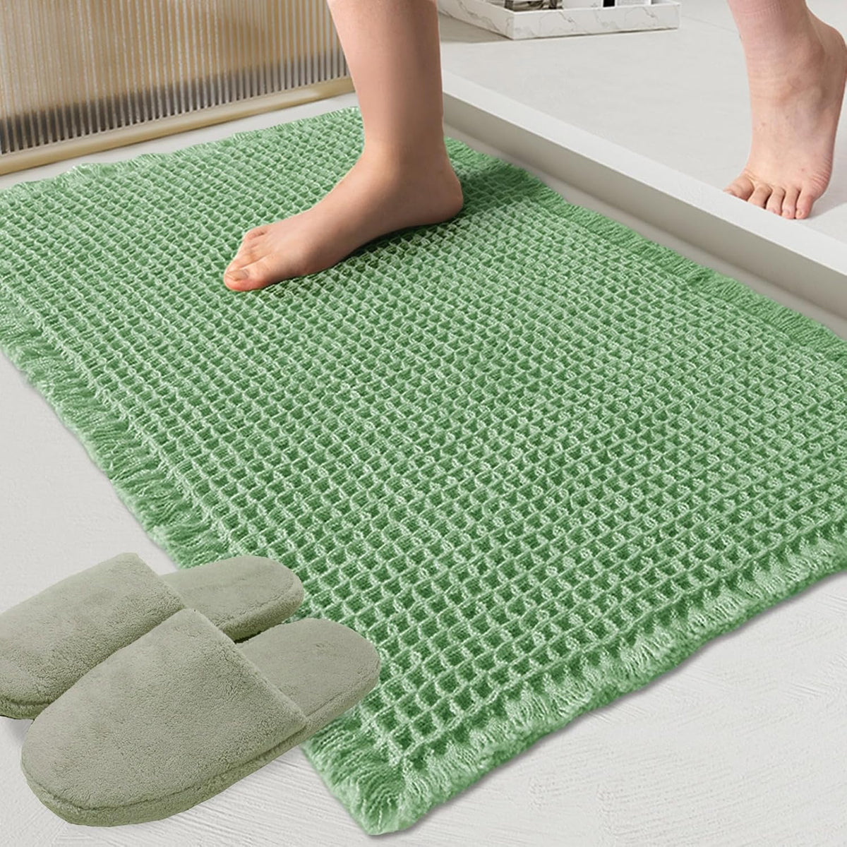 Close-up of a green waffle bath mat with a bare foot stepping onto it and slippers nearby.