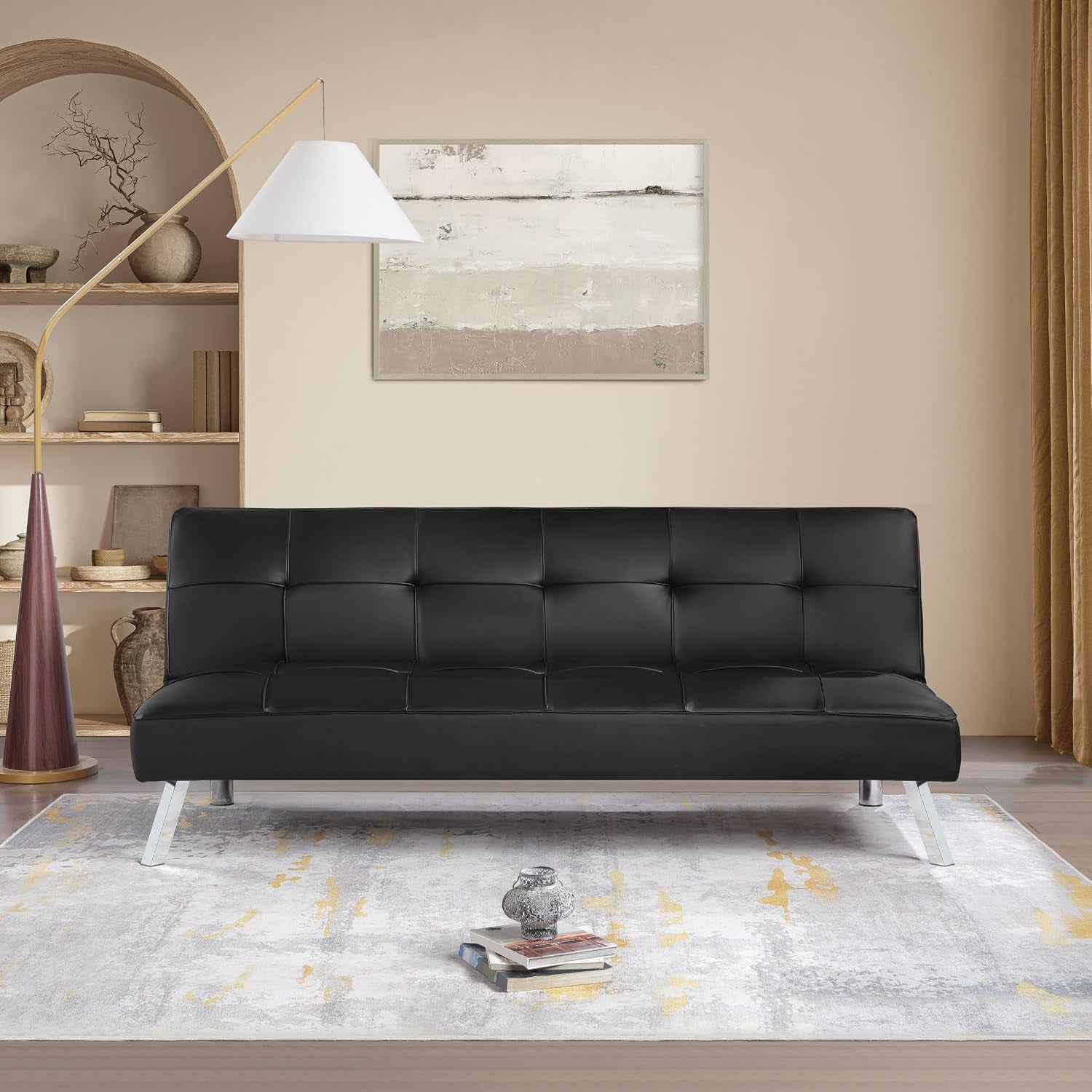 Black faux leather futon sofa in a styled living room setting with chrome legs and tufted back