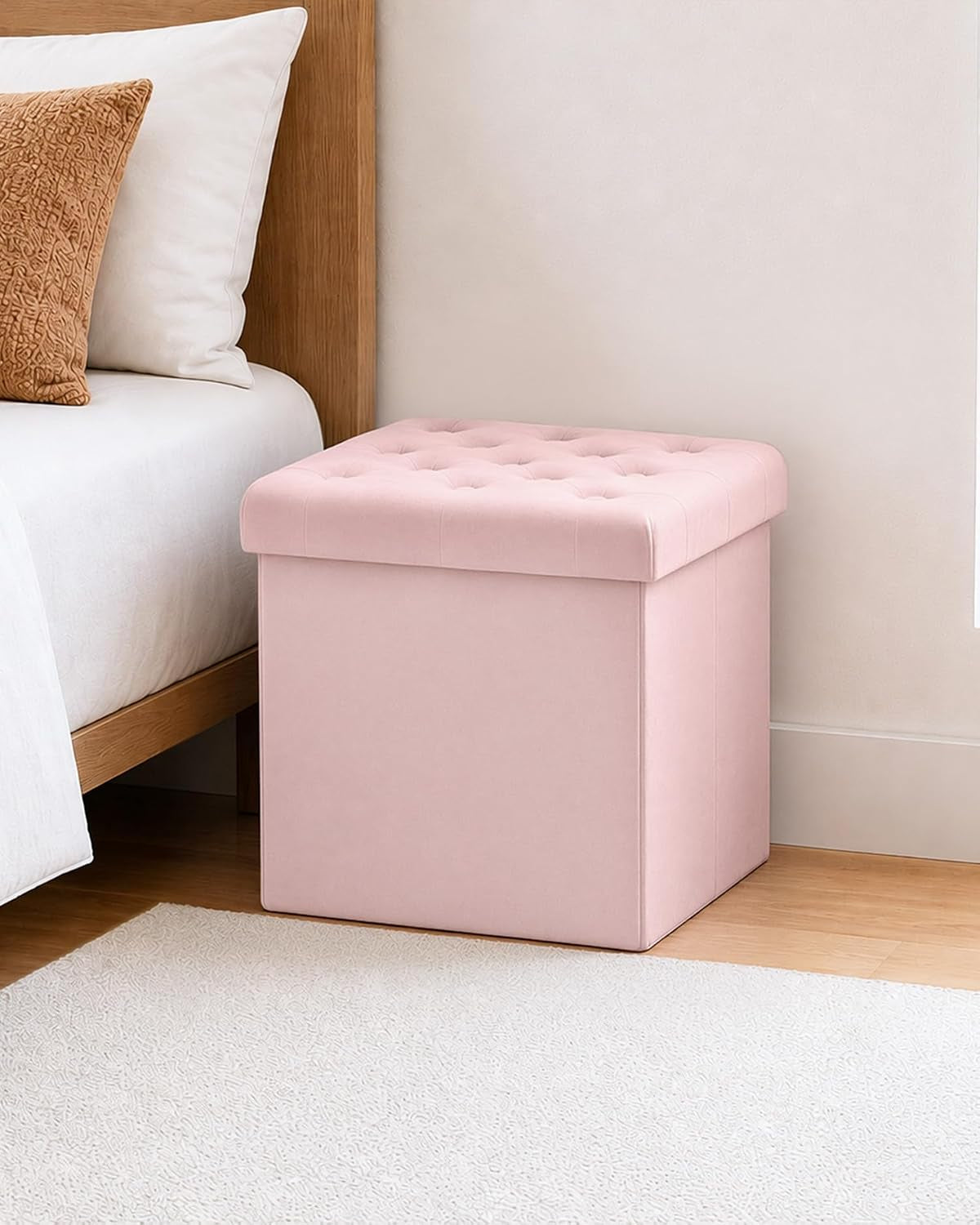 Pink tufted square storage ottoman placed on the floor next to a bed