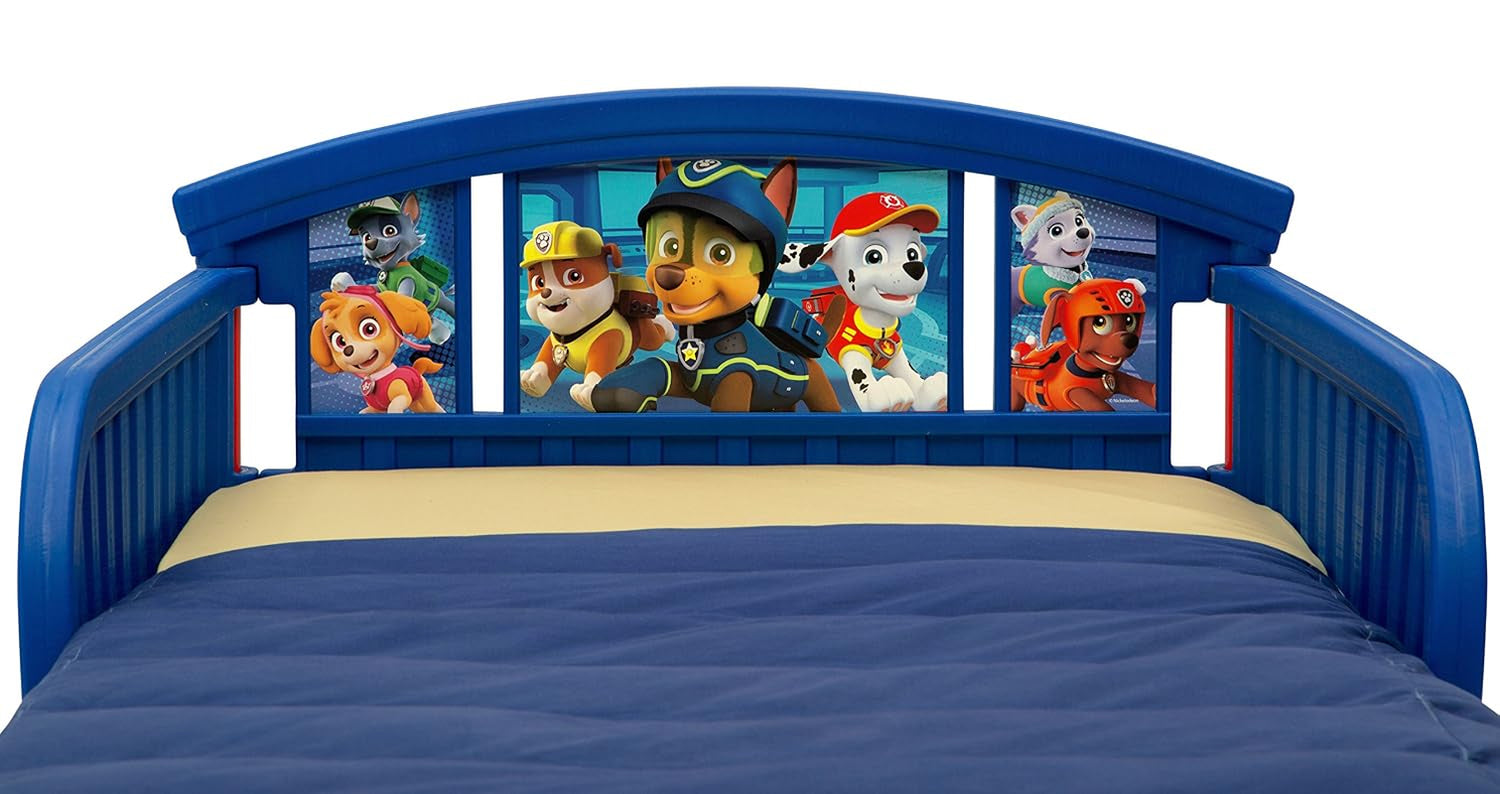 Close-up of blue plastic toddler bed headboard with colorful Paw Patrol character panels and navy bedding.