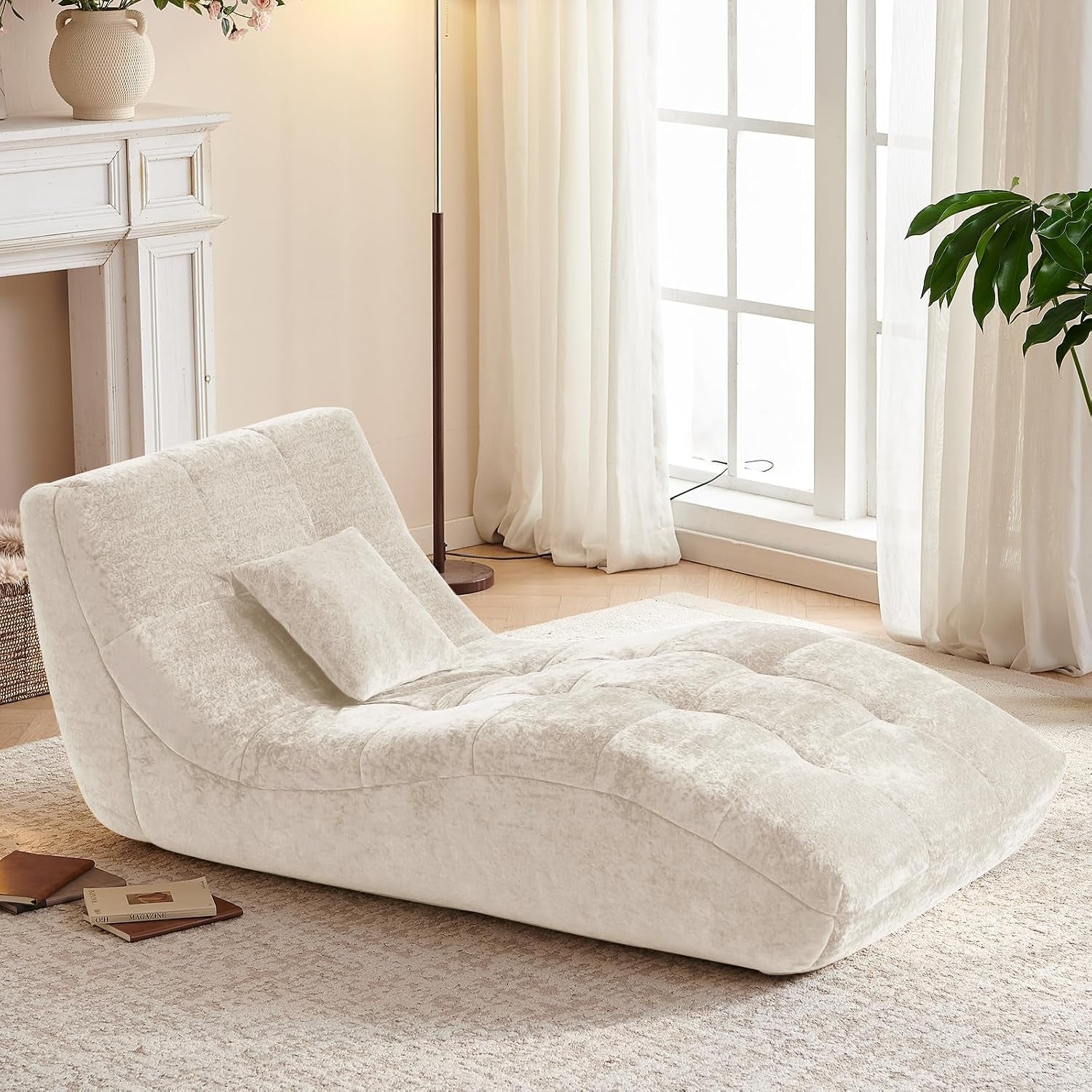 Three-quarter view of the beige chaise with matching pillow beside a tall floor lamp.