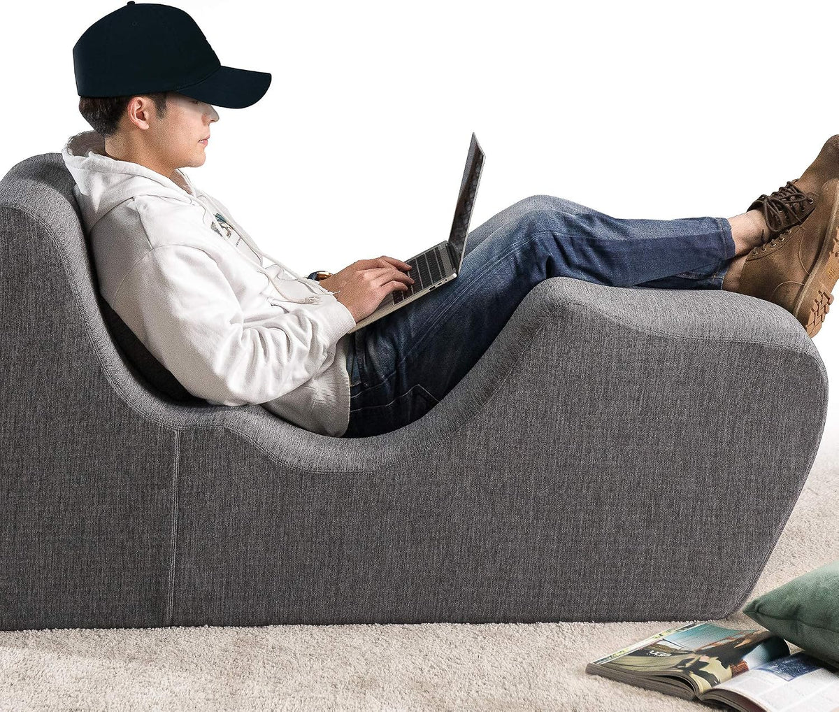 Person reclining on dark grey chaise lounger using a laptop in a casual living room setting, side view