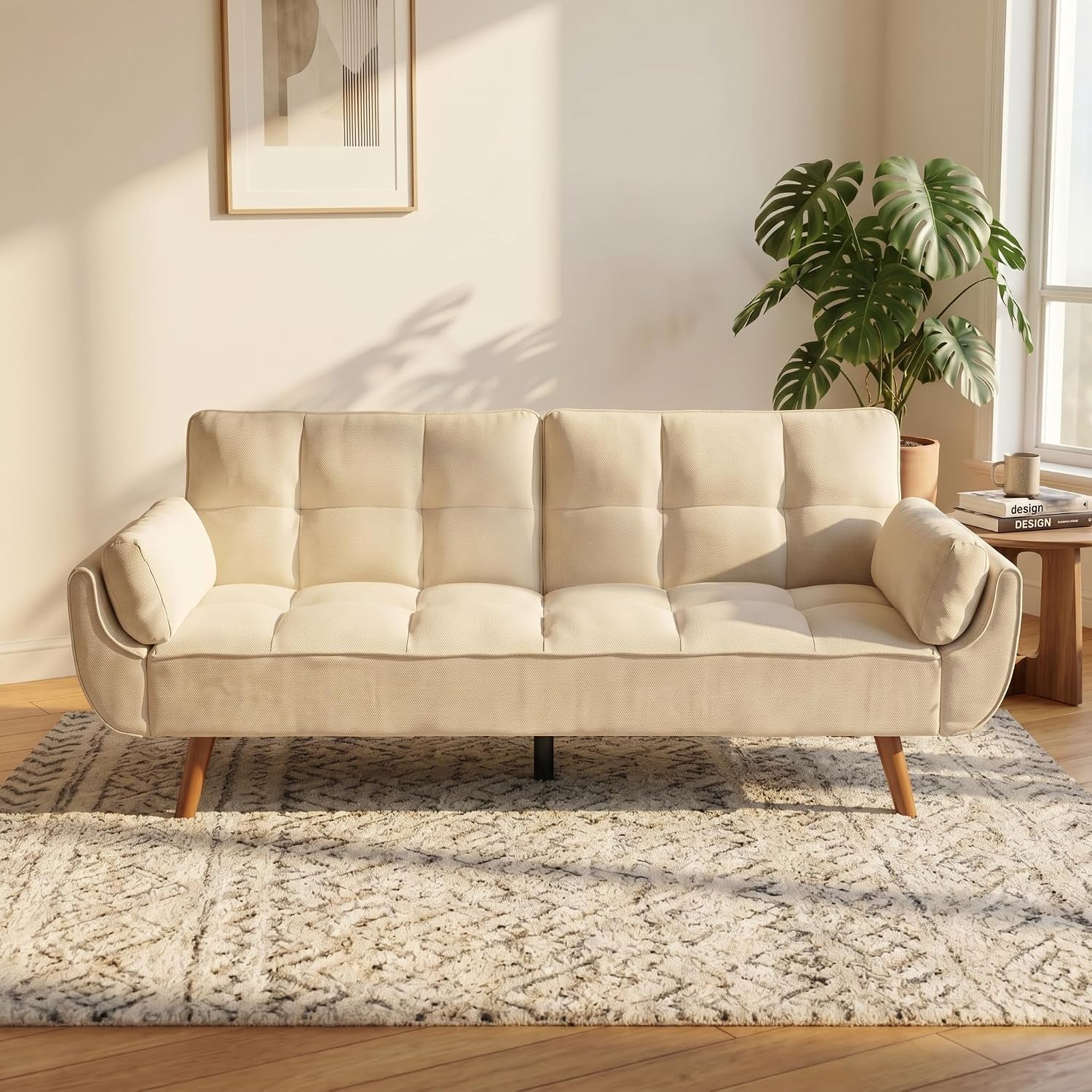 Cream-beige tufted sofa bed with rolled arm bolsters set on a patterned rug near a window.