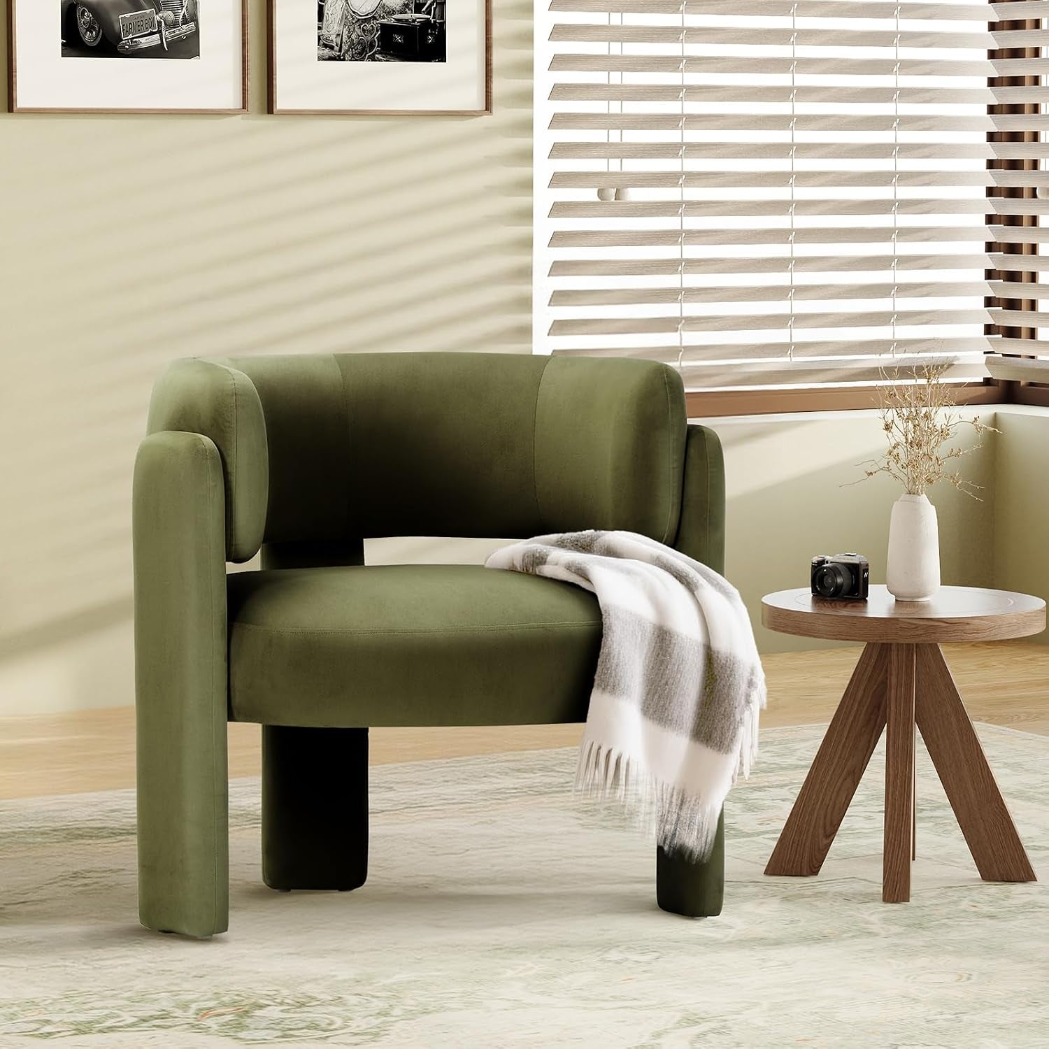 Olive green velvet barrel chair with throw draped over seat next to a tripod wood side table