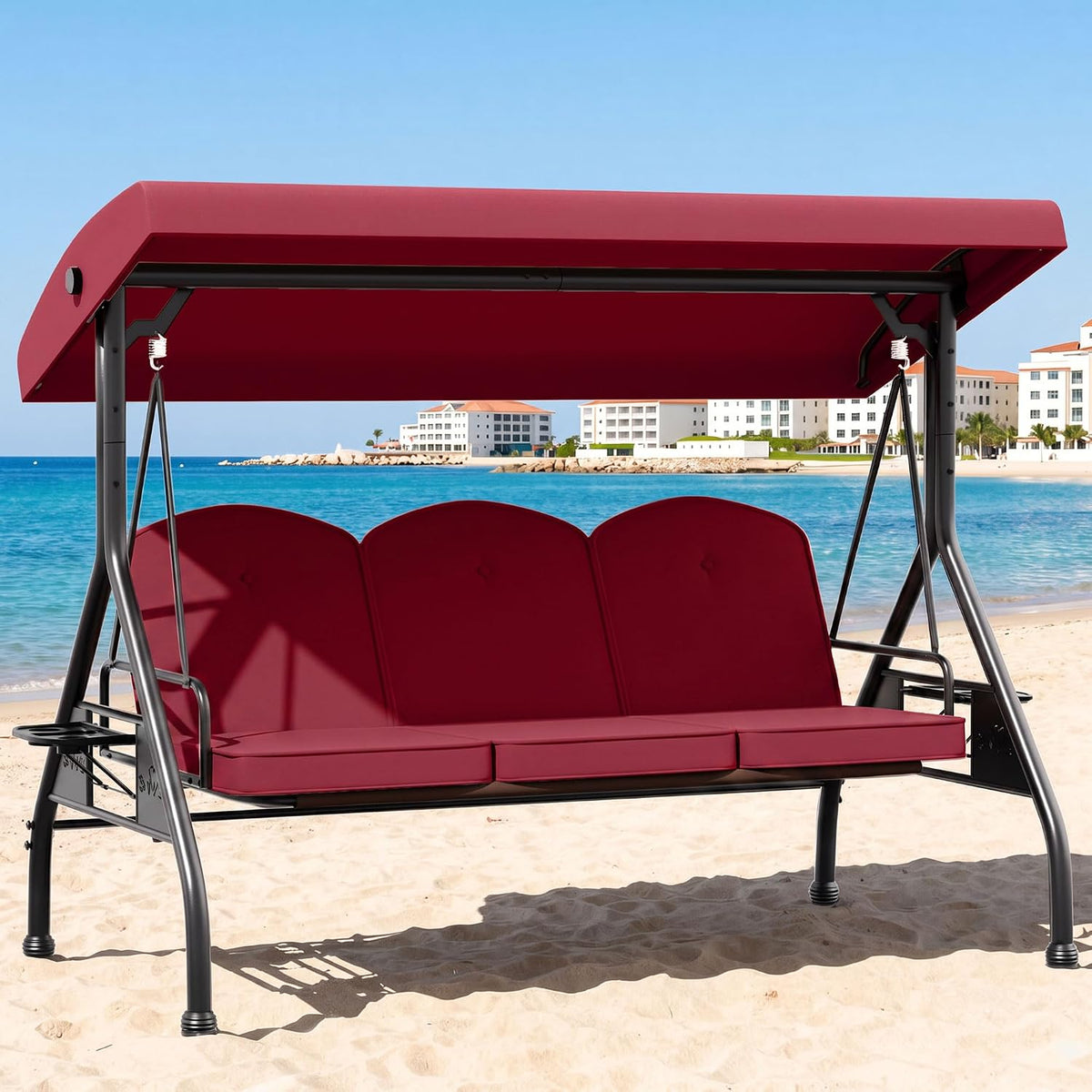 Three-seat outdoor swing with adjustable canopy and red cushions set on a sandy beach.