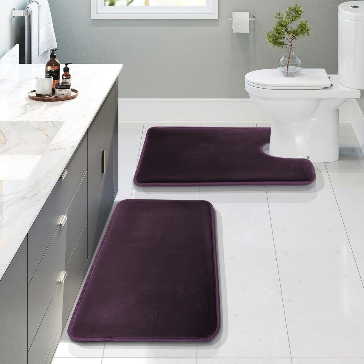 Deep plum rectangular and U-shaped mats laid on white tile next to a grey vanity, showing low shadows and rounded piped