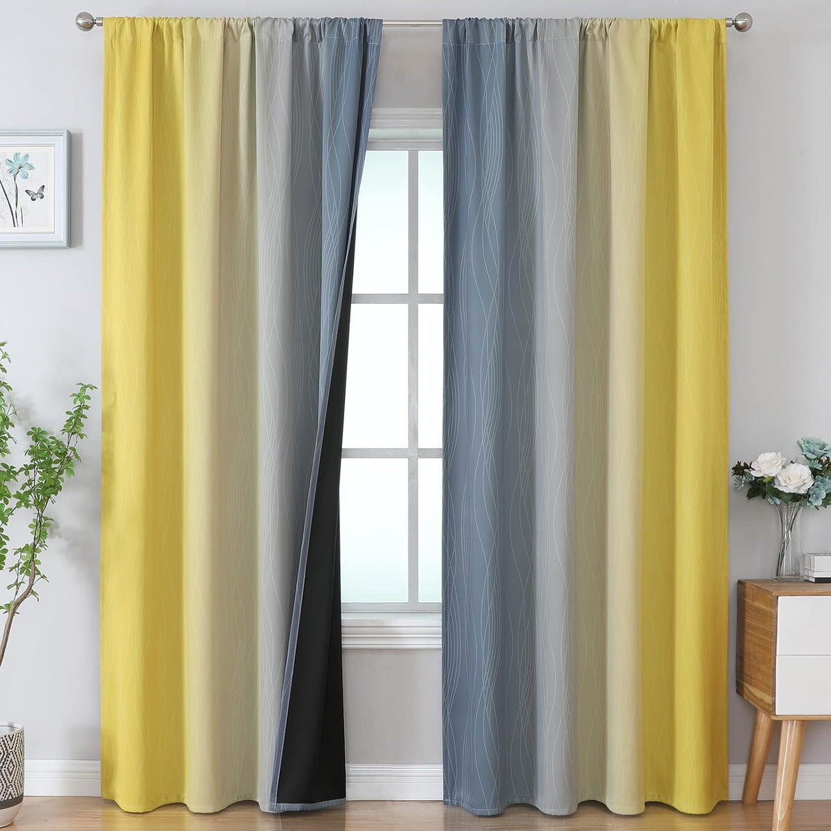 Pair of yellow-to-gray ombre curtains hung on a rod with a styled plant and nightstand beside.
