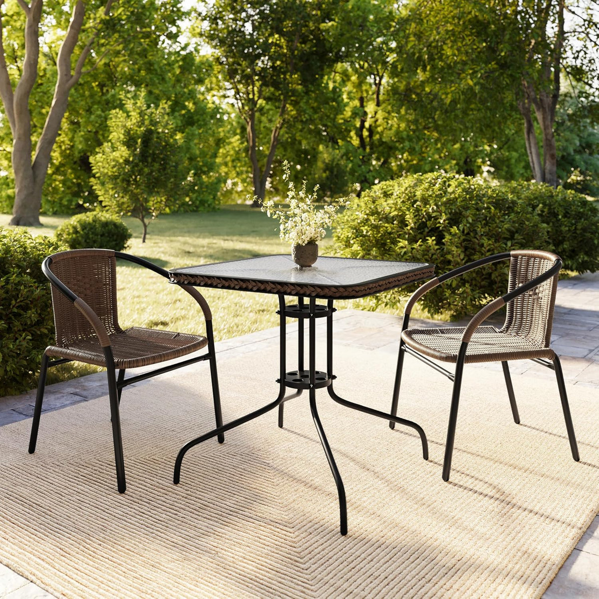 Pair of brown rattan dining chairs with black frames arranged around a square patio table on a rug in a garden setting