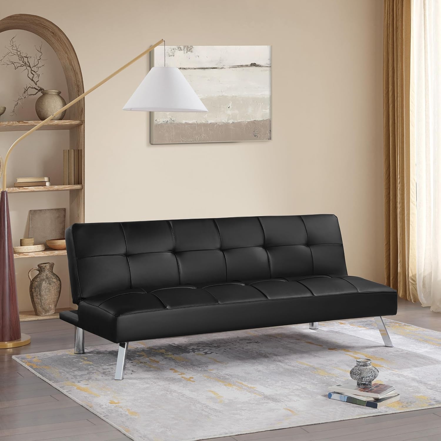 Living room shot of a black tufted faux-leather futon sofa with angled chrome legs on a light area rug.