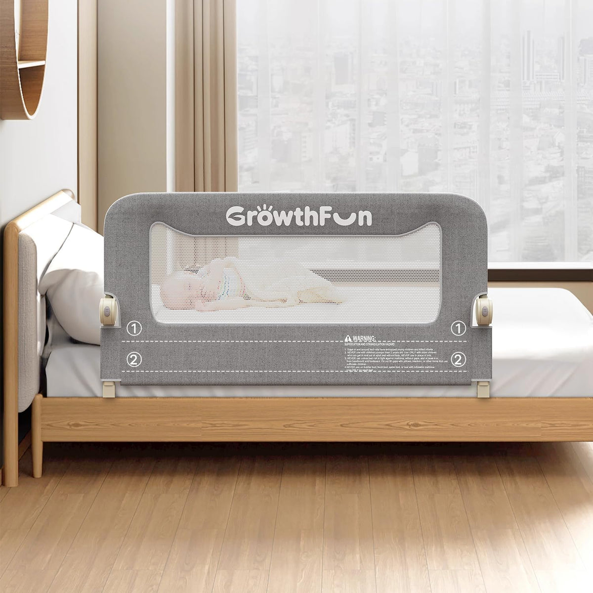 Front view of a dark gray bed rail with mesh panel and mounting feet on a wood bed in a bright bedroom
