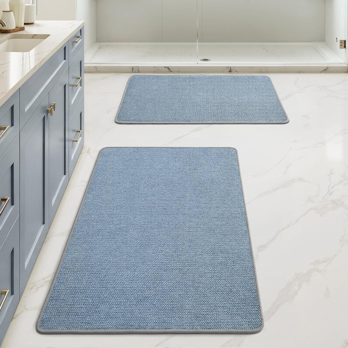 Bathroom with two textured light blue rectangular mats laid in front of shower and sink cabinet.