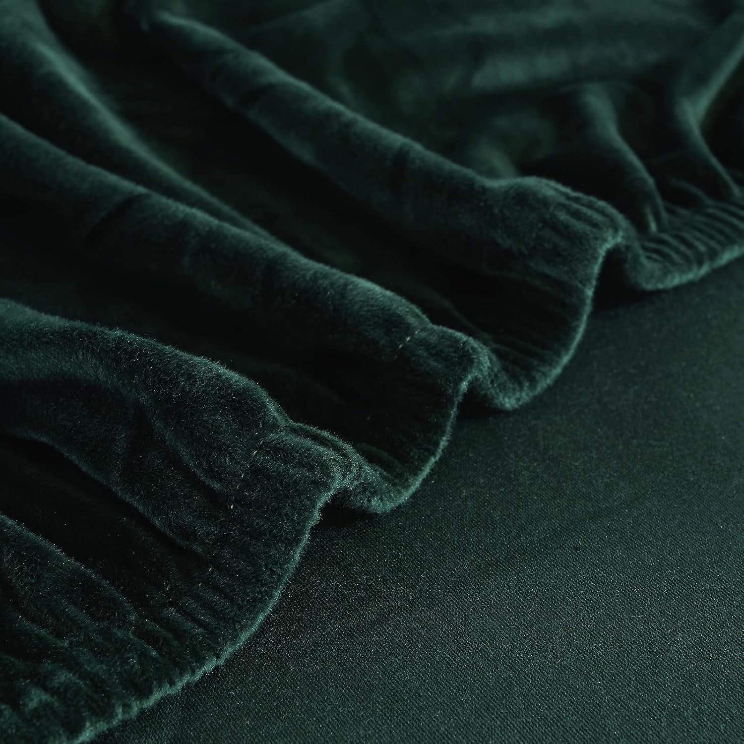 Dark green velvet slipcover hem and elastic edge close-up showing gathered fabric and stretch edge