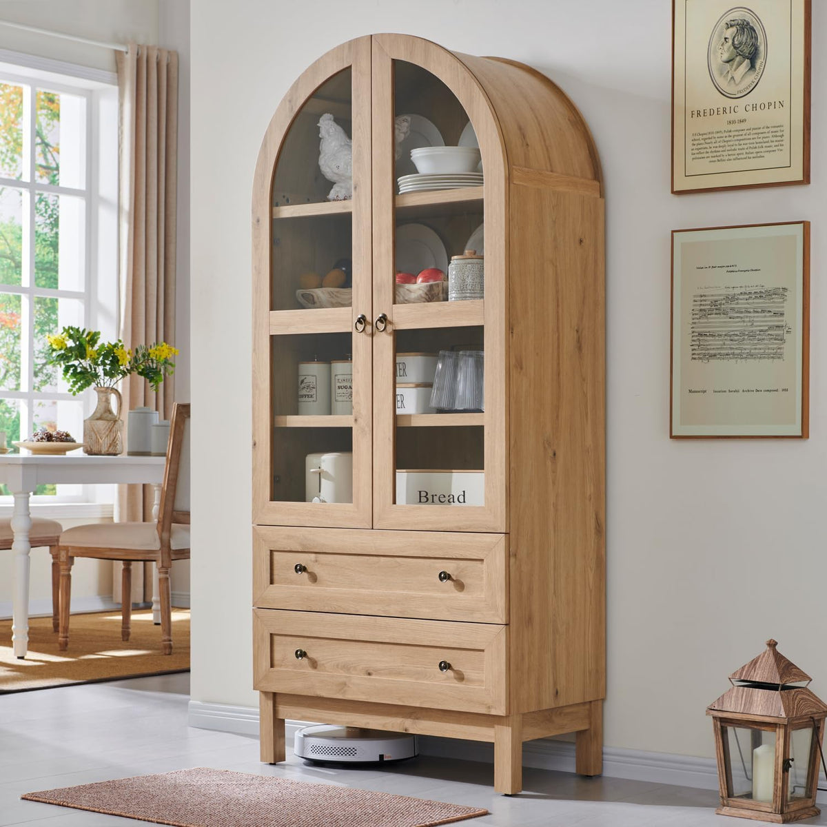 Straight front view of arched pantry cabinet in natural finish placed in a dining-kitchen area with robot vacuum underneath