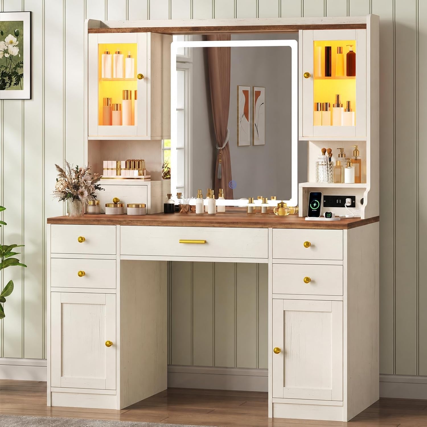 Light wood-topped vanity with warm yellow cabinet lighting and a framed mirror against green paneled wall.