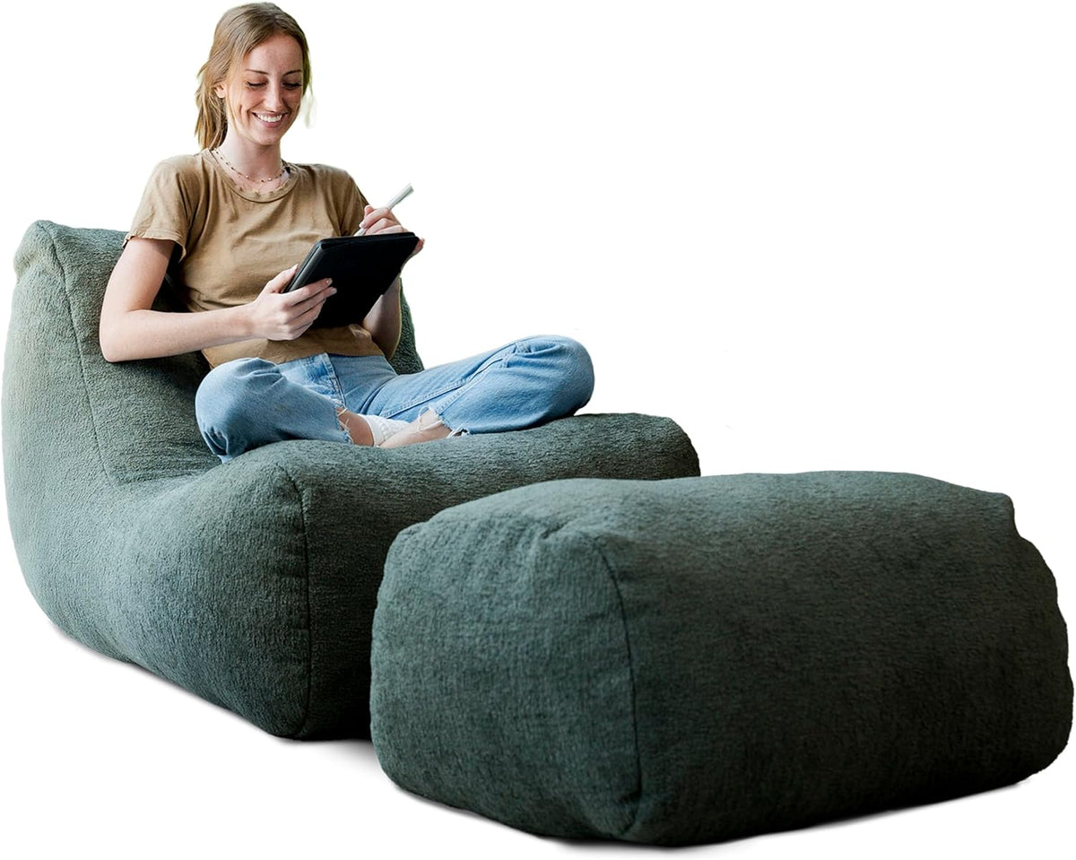 Front-left view of a dark green lounge chair and matching ottoman with a person sitting cross-legged using a tablet.