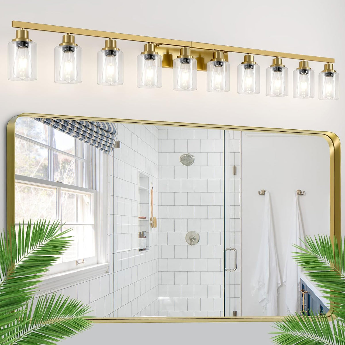 Long ten-light brushed gold vanity bar with clear shades mounted above a large mirror reflecting a tiled shower.