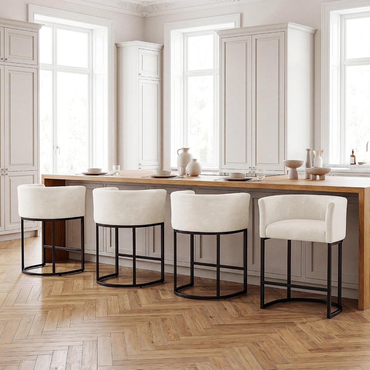 Four off-white chenille counter stools with curved backs and dark metal bases lined up under a long wooden counter in a