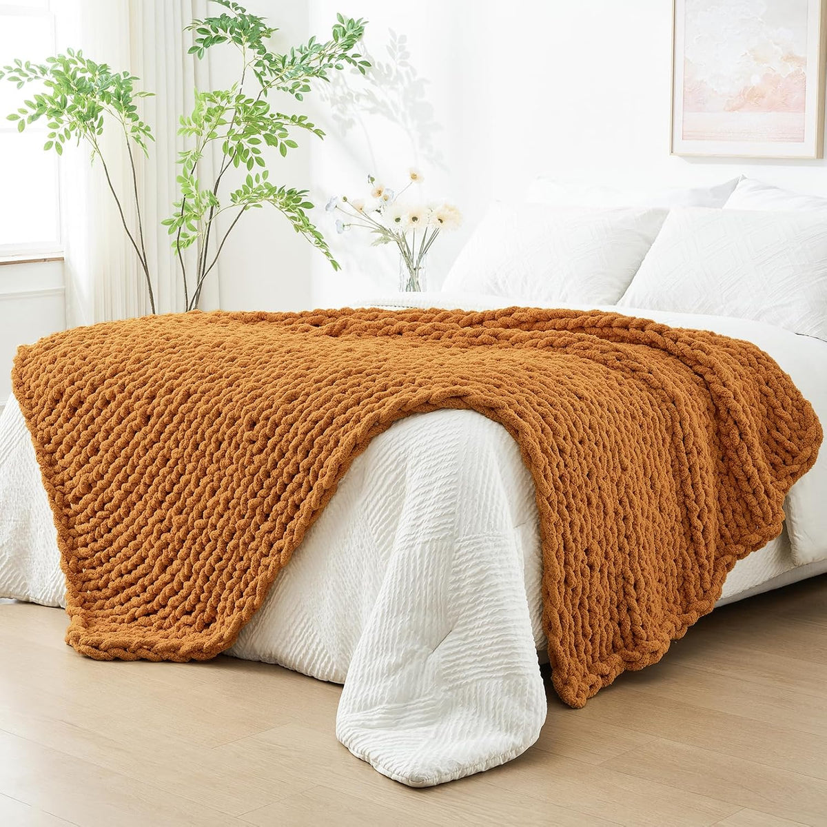 Burnt orange chunky knit throw spread across the center of a white bed, edges hanging over
