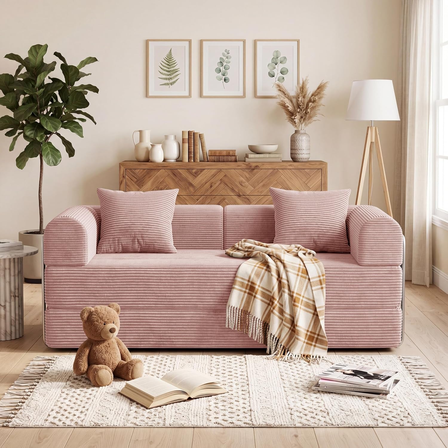 Pink corduroy convertible sofa with two matching pillows and a plaid throw in a bright living room.