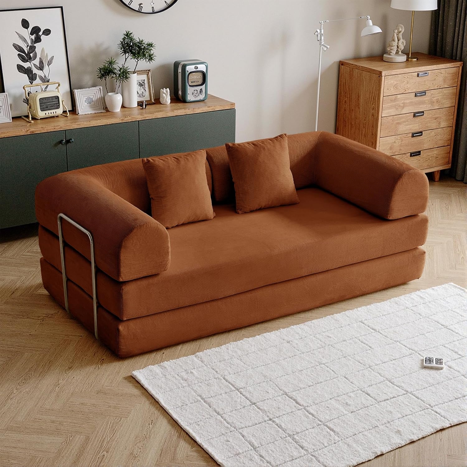 Rust-colored corduroy sofa in sofa position with three pillows and metal side rails in a warm-toned room.