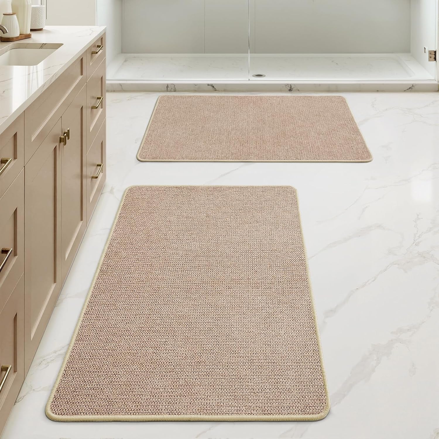 Bathroom floor with two rectangular beige mats placed in front of a shower and vanity.