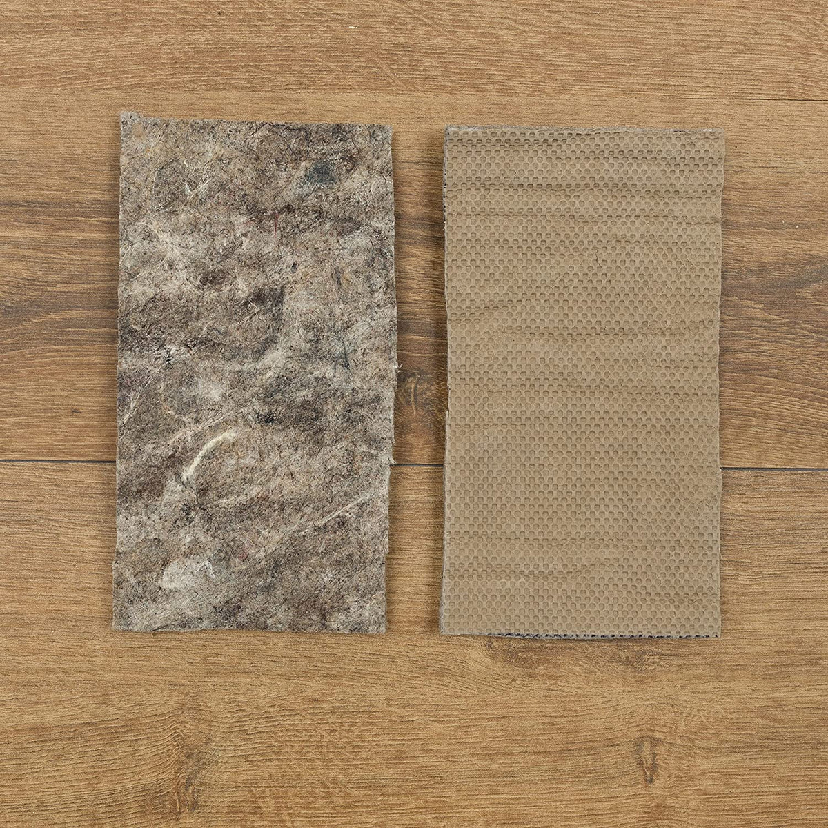 Two rectangular pad samples side-by-side: mottled felt piece at left and honeycomb-textured gripper at right on wood.