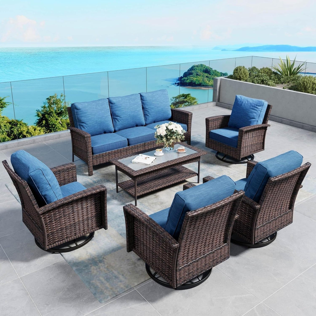 Seven-piece brown wicker patio set with blue cushions arranged around a rectangular coffee table on a coastal balcony.