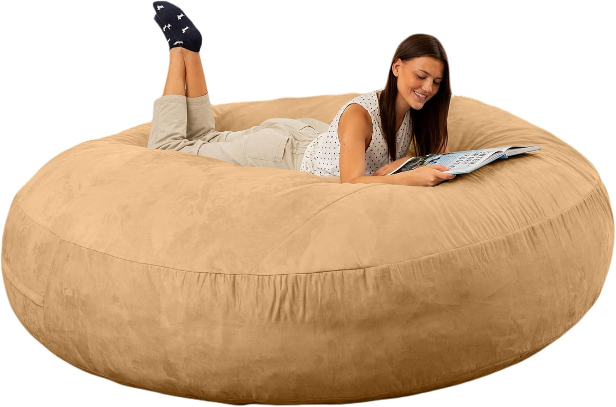 Woman lying on her stomach reading on a large tan round bean bag bed with feet raised