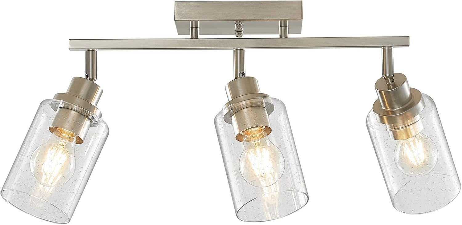 Three-light brushed nickel track fixture shown straight-on with seeded glass cylinders and lit bulbs