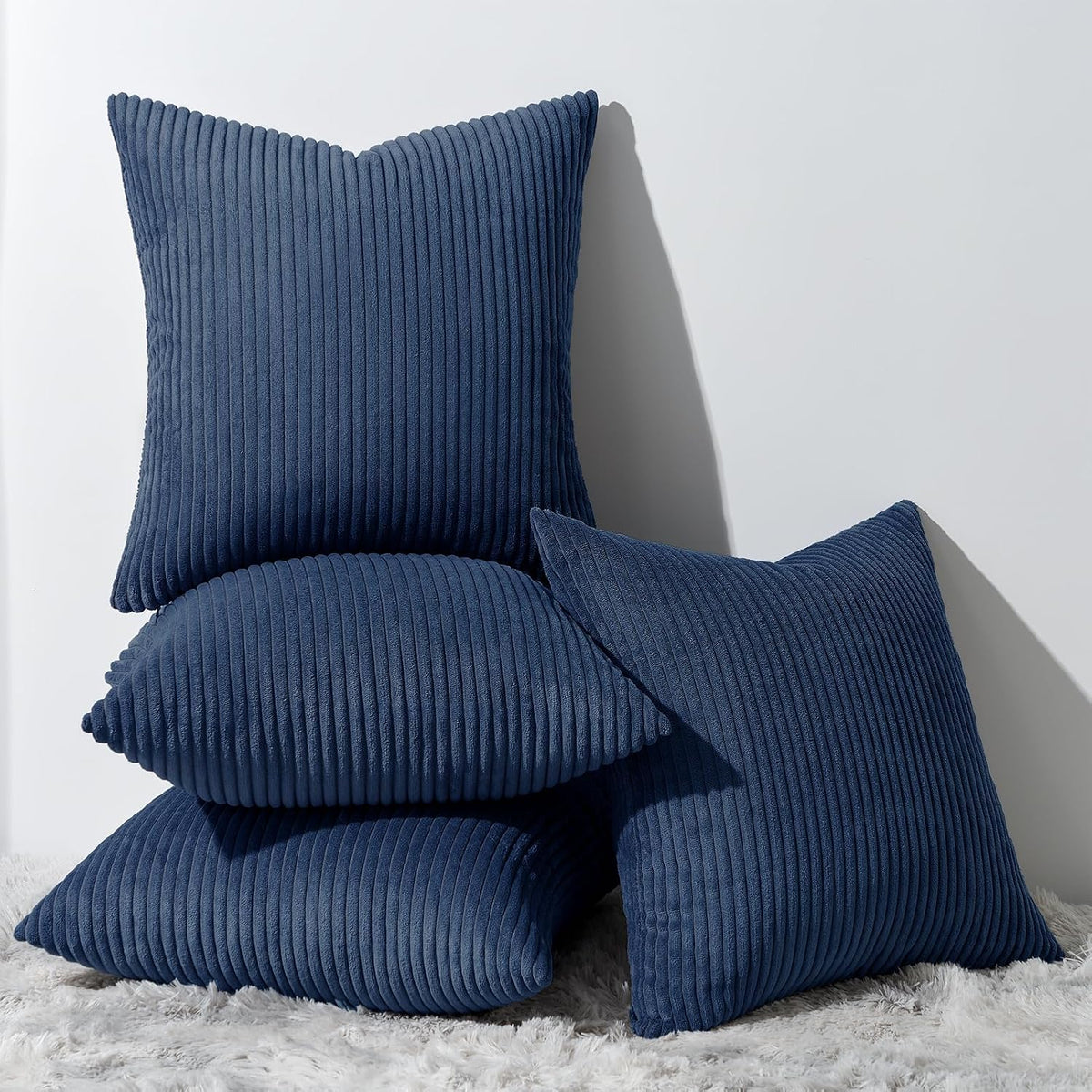 Pile of vertically ribbed square pillows in deep navy blue on a textured rug