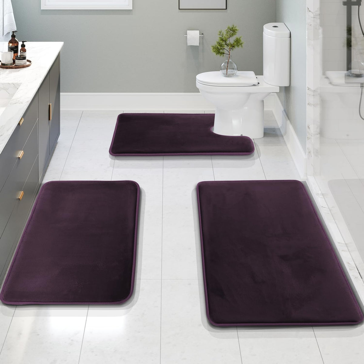 Bathroom view showing three deep-plum velvet mats—two rectangular runners in the foreground and a U-shaped mat at the toilet
