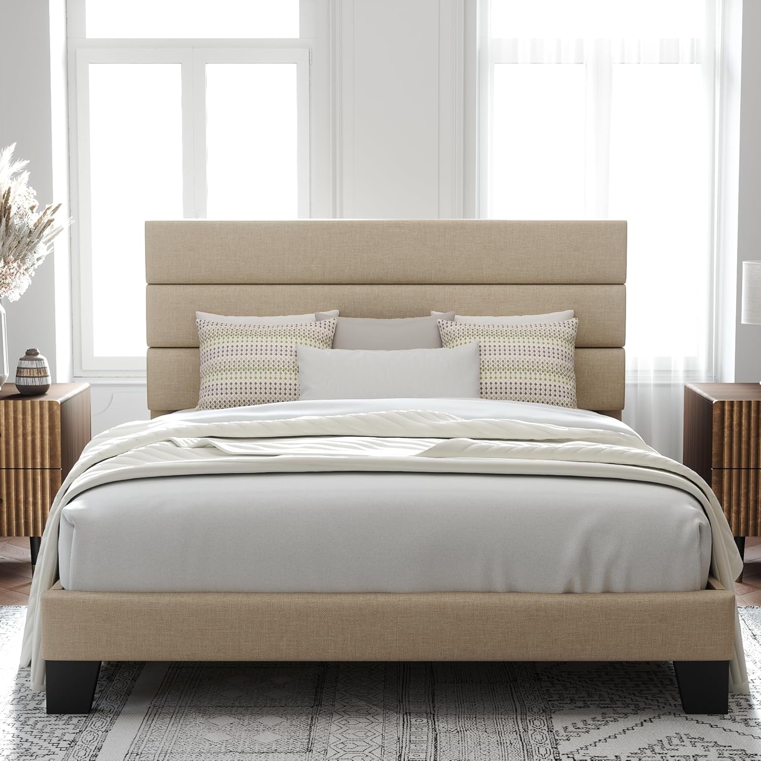 Centered bedroom view of a beige upholstered bed with white bedding and black feet.