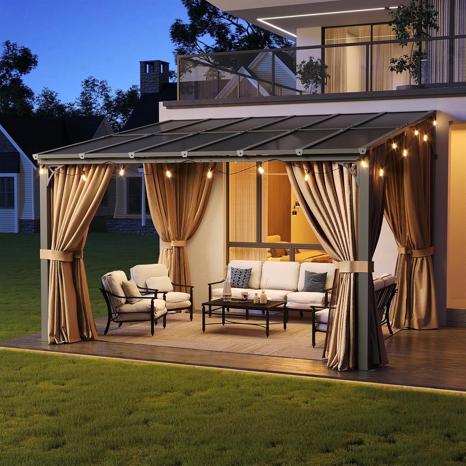 Evening view of a wall-mounted pergola with tied-back curtains, lit string lights and cushioned seating beneath.