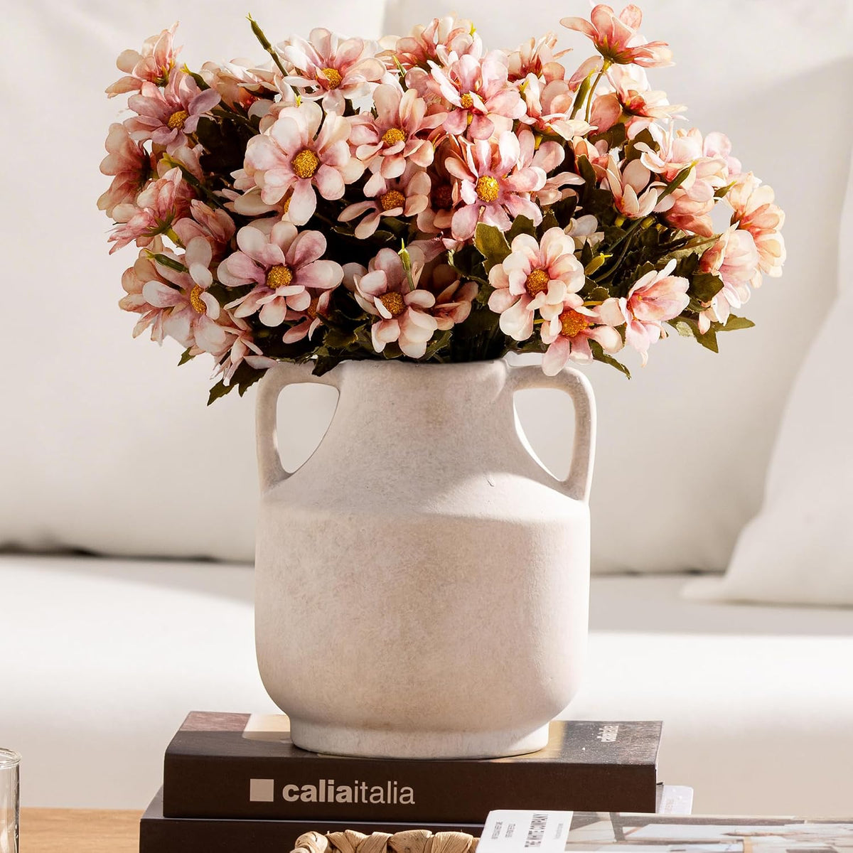Close crop of a small handled vase topped with a dense bouquet of pink daisy-like flowers