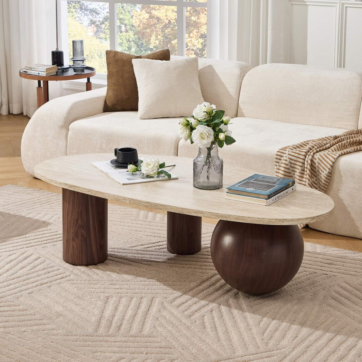 Oval coffee table with beige top and walnut-finish legs placed in a bright living room beside a cream sofa