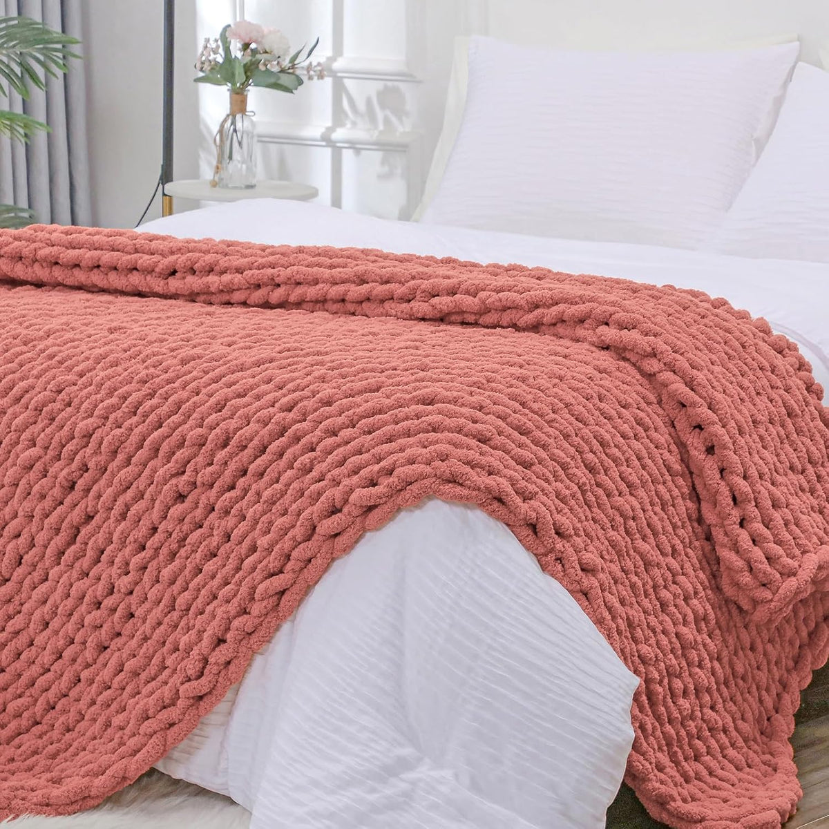 Close-up view of a coral chunky knit throw folded on a white bed showing thick braided texture.