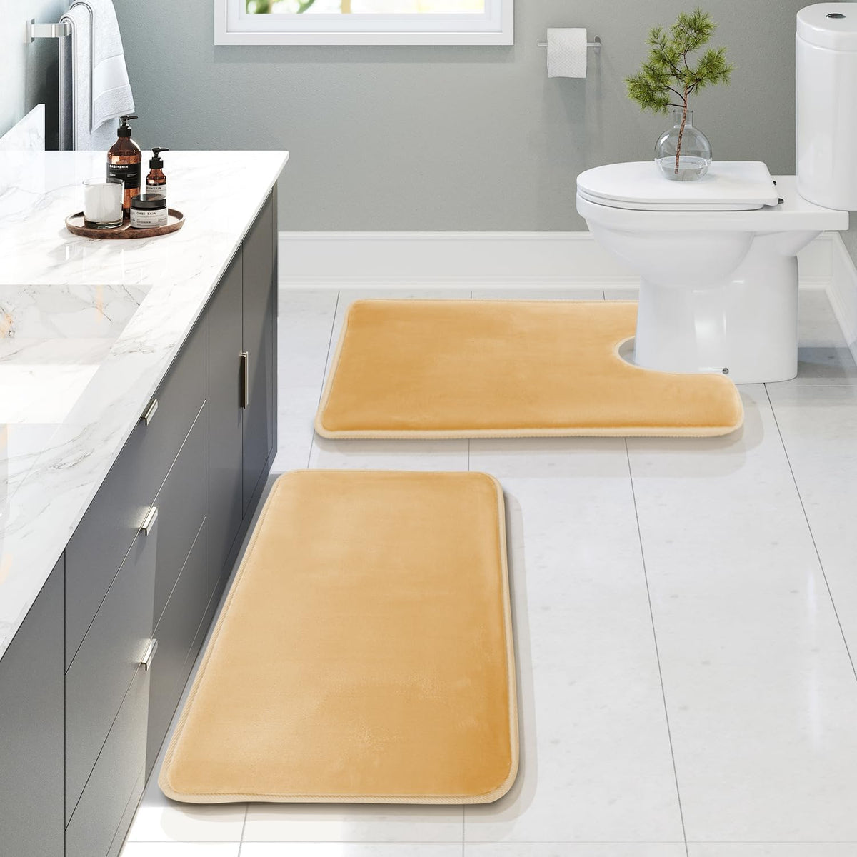 Angled view from the vanity showing two golden bath mats with the U-shaped contour mat at the toilet.