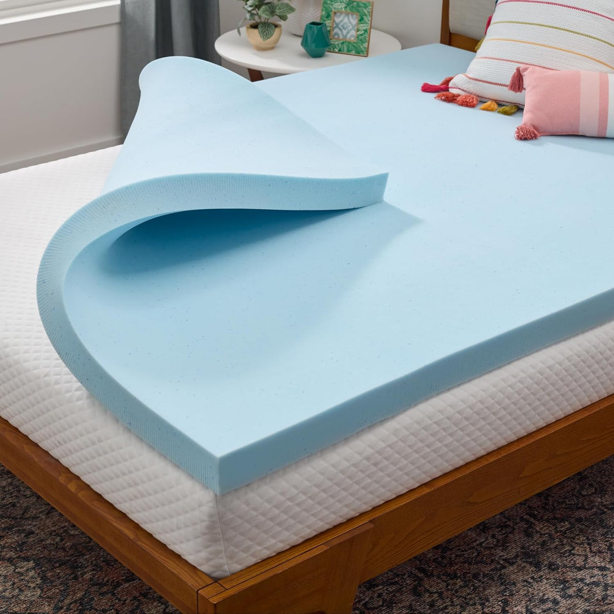 Close-up corner view of a light blue memory foam topper folded back on a bed