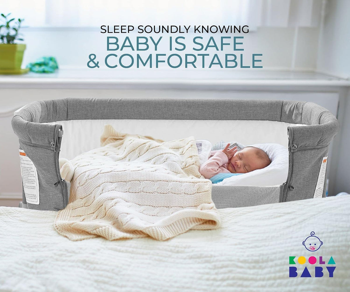 Gray bedside sleeper attached to a bed with a sleeping infant covered by a knit blanket