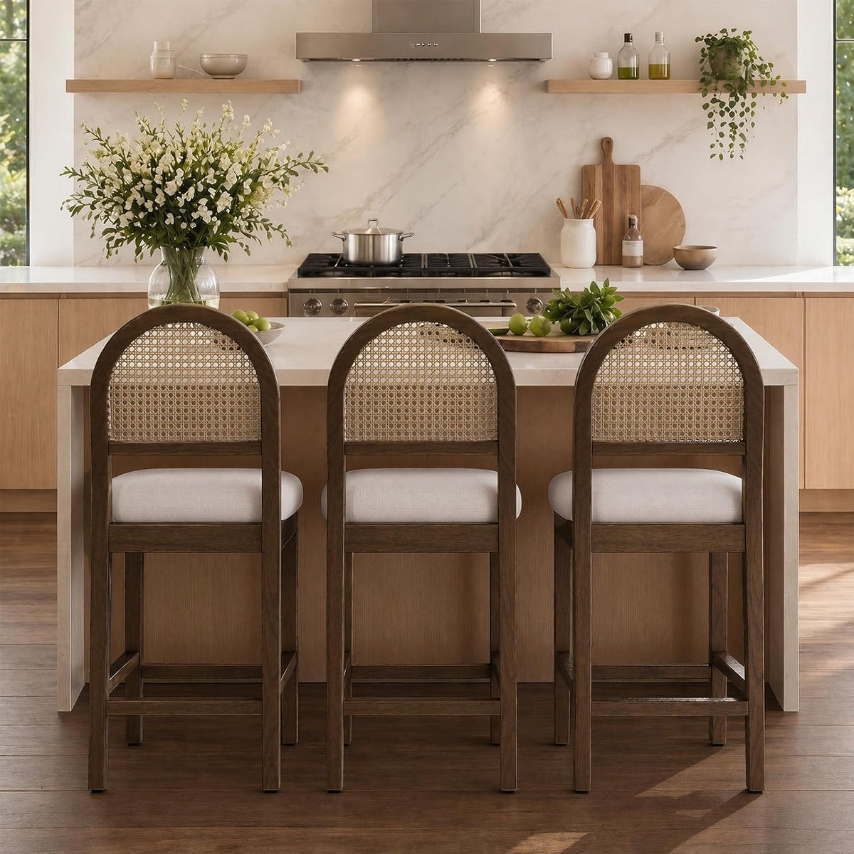 Three counter-height stools with cane backs and white chenille seats seen from behind at an island and stove backdrop