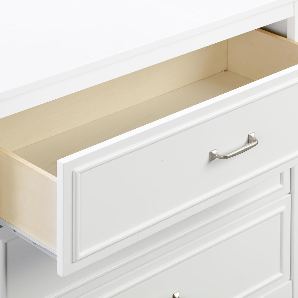Close-up of the top drawer pulled out showing light wood interior and the silver metal drawer handle on the white front.