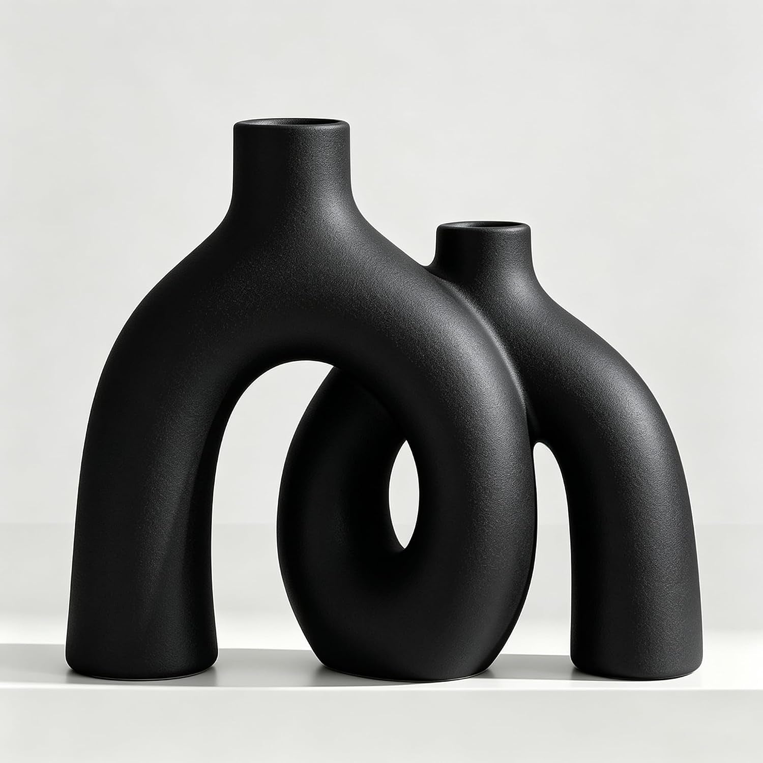 Close view of two matte black donut-shaped ceramic vases arranged together