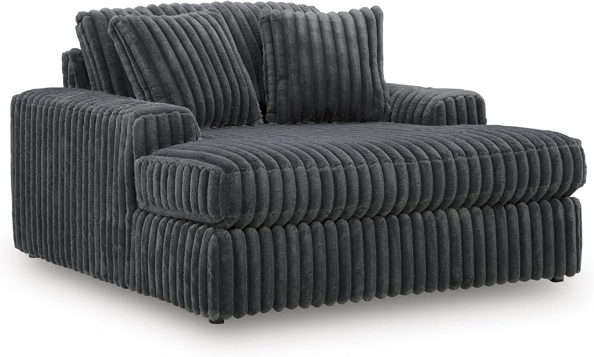Angled side view of a charcoal-gray oversized chaise chair with matching ribbed pillows.