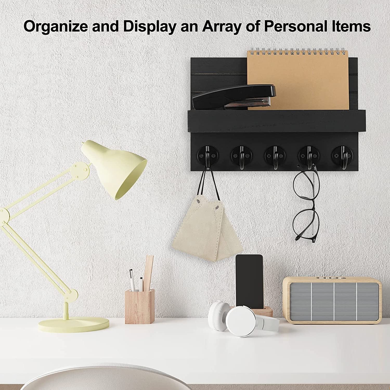 Black wall organizer above a desk, holding a notebook, stapler, face mask, and eyeglasses.