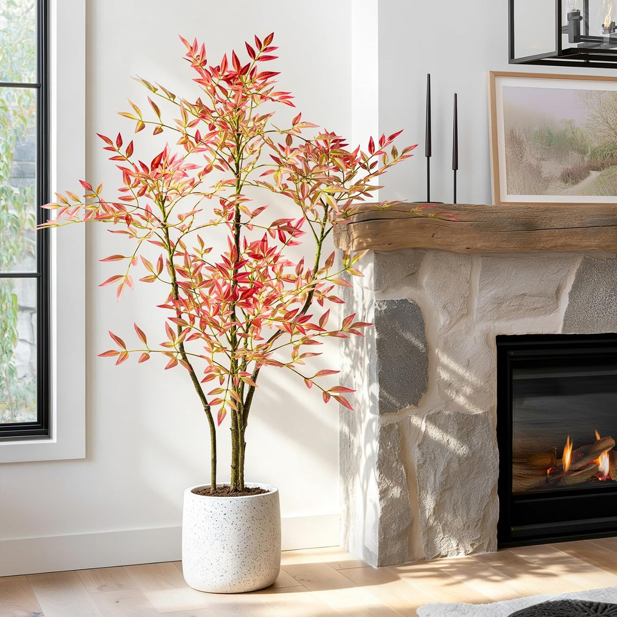 Faux nandina with red-tinted leaves beside a rustic stone fireplace and a wooden mantel with tall candle sticks.
